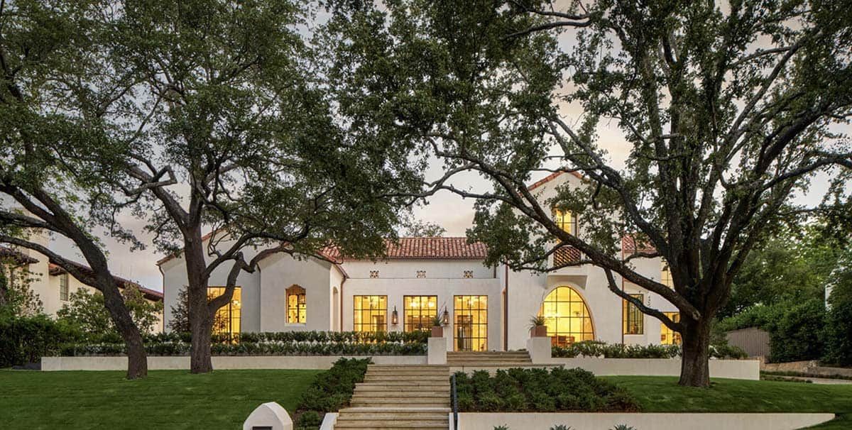 Twilight exterior of Spanish Colonial Revival home in Texas with illuminated windows