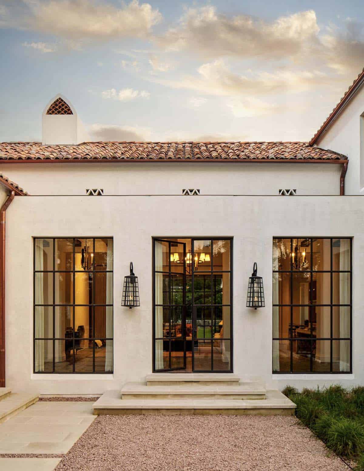 Spanish Colonial Revival home in Texas with steel French doors and lantern sconces at dusk