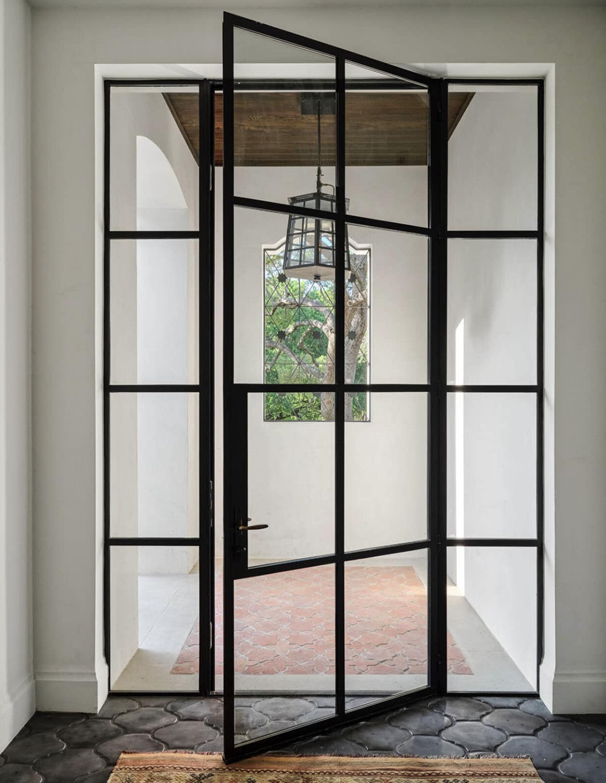 Pivoting steel and glass front door in Spanish Colonial Revival home entryway