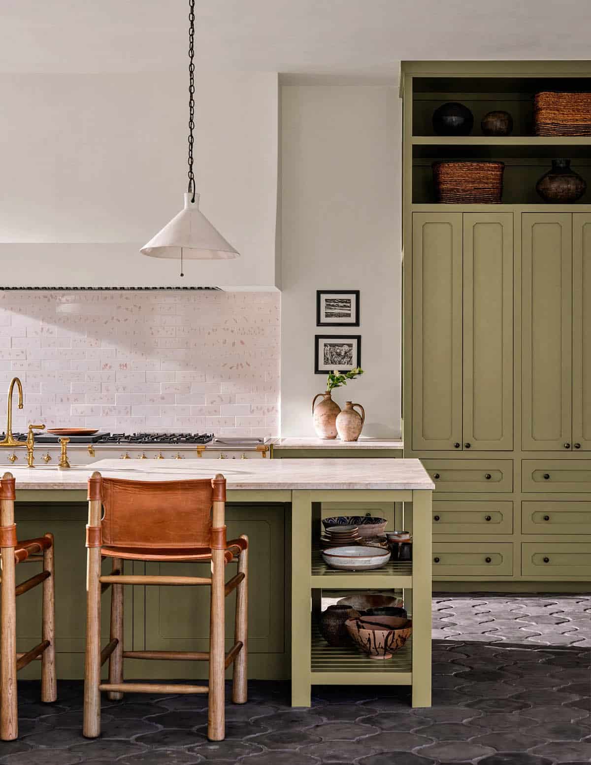 Sage green kitchen cabinetry with brass hardware and leather counter stools
