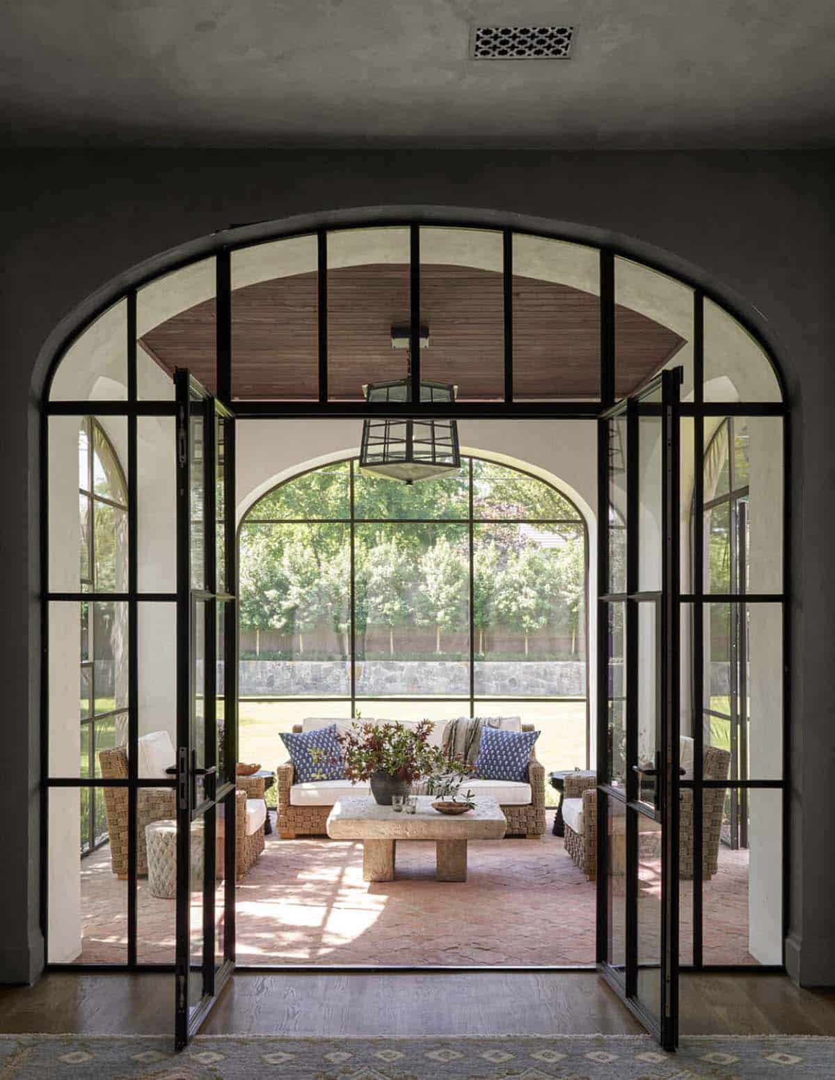Arched steel doors opening to screened porch with woven furniture