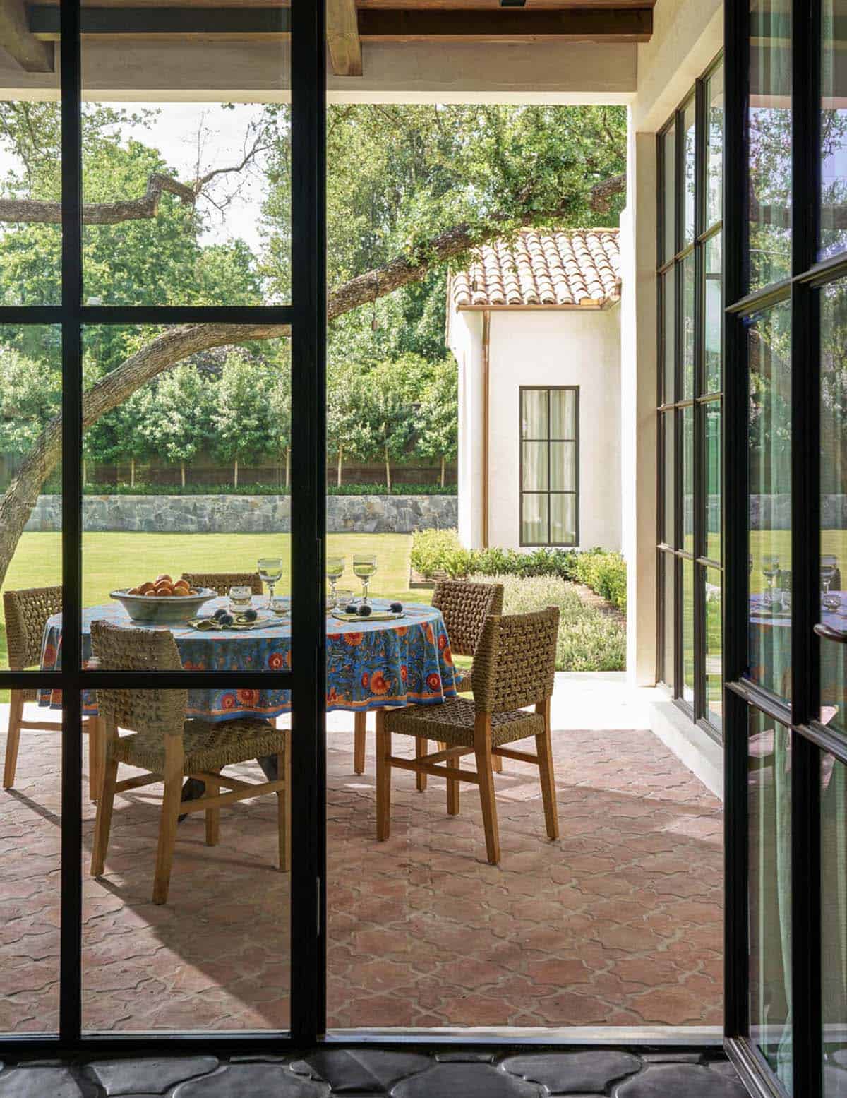 Covered patio with steel doors framing dining table and oak tree