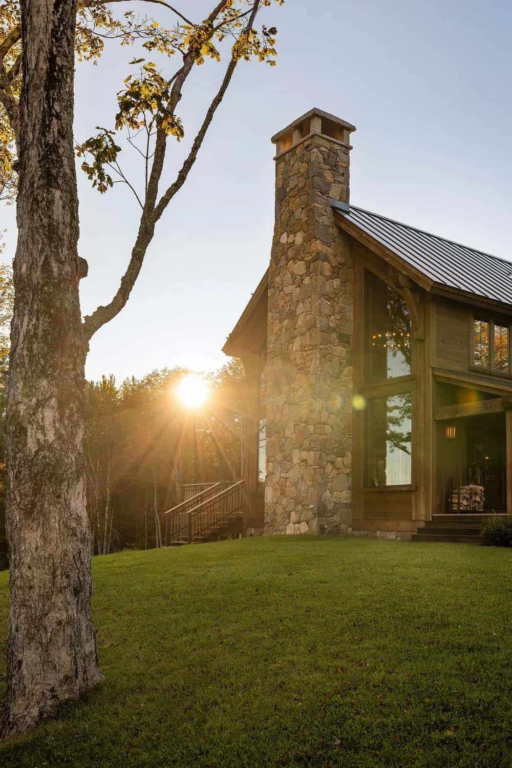 Stone chimney and metal roof glowing in autumn sunset light through trees