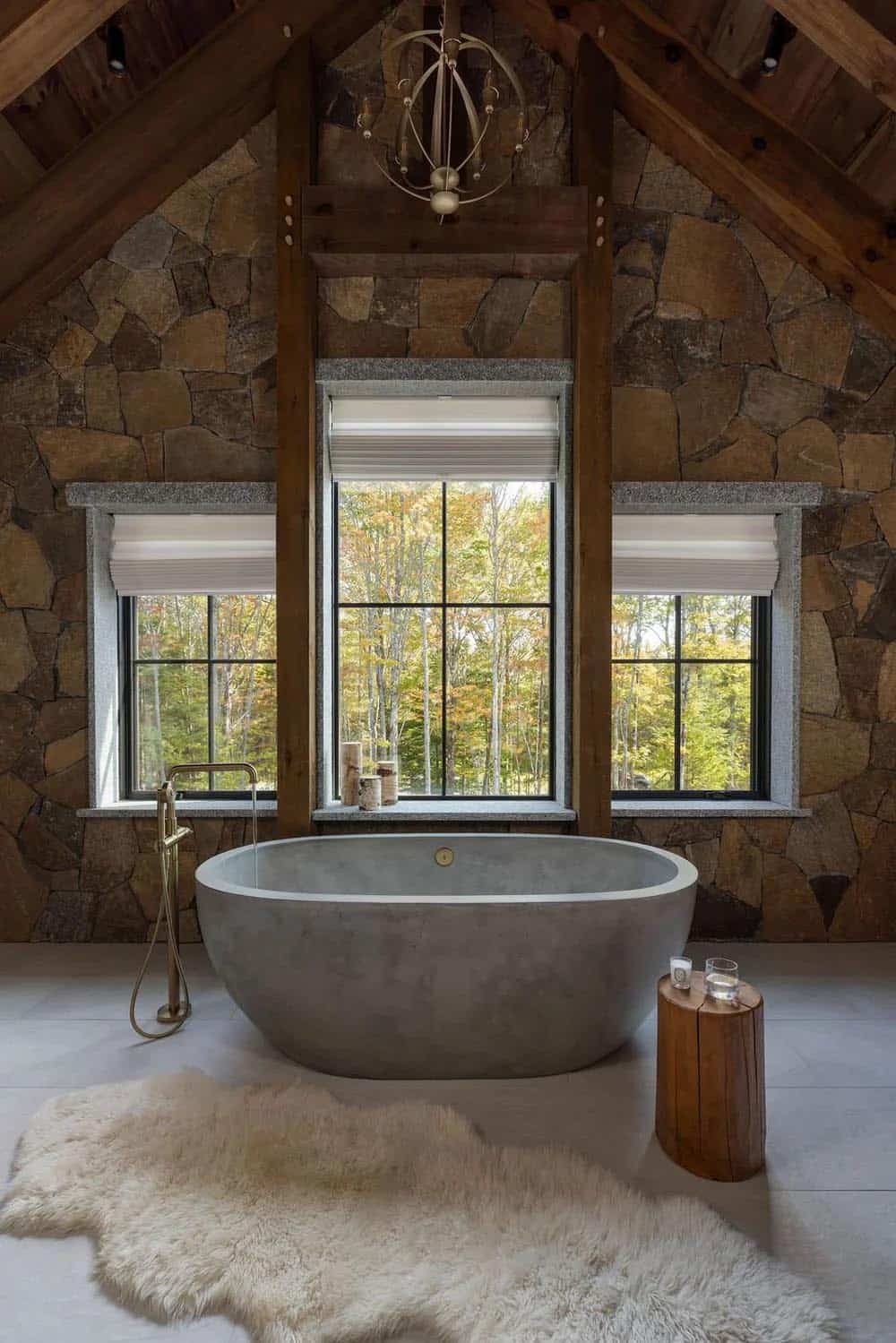 Primary bathroom with freestanding concrete tub against stone wall and forest views