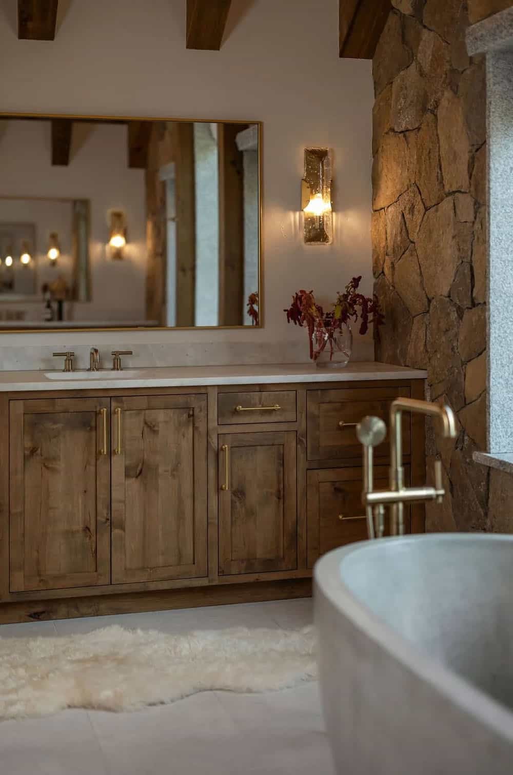 Bathroom vanity with wood cabinetry, brass fixtures, and stone accent wall