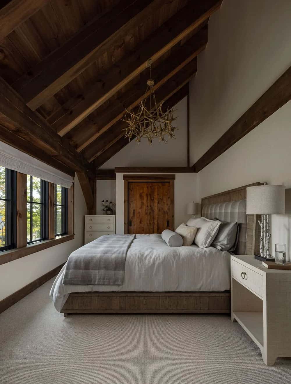 Bedroom with vaulted wood ceiling, antler chandelier, and upholstered headboard
