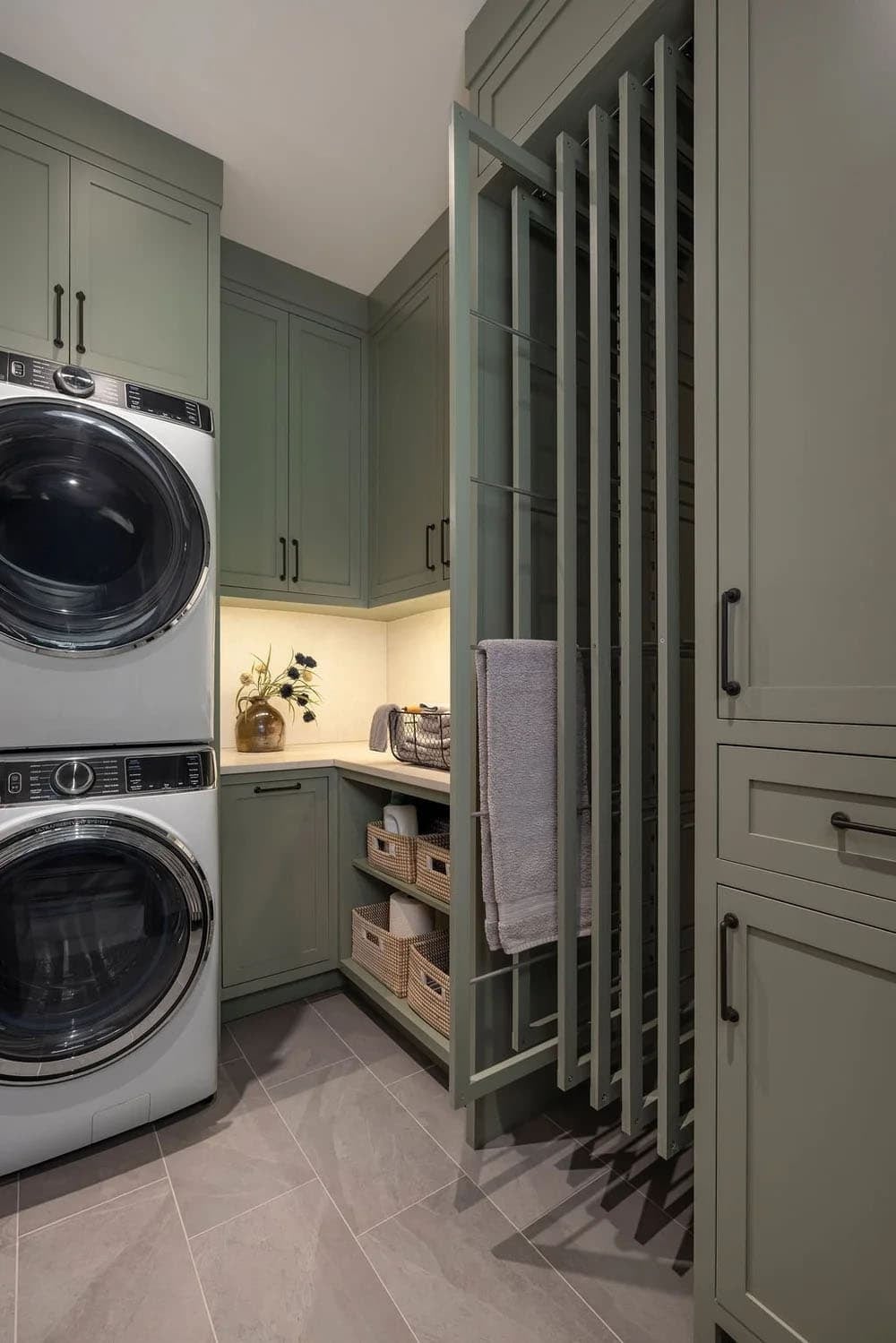 Laundry room with sage-green cabinetry, stacked washer-dryer, and pull-out drying rack