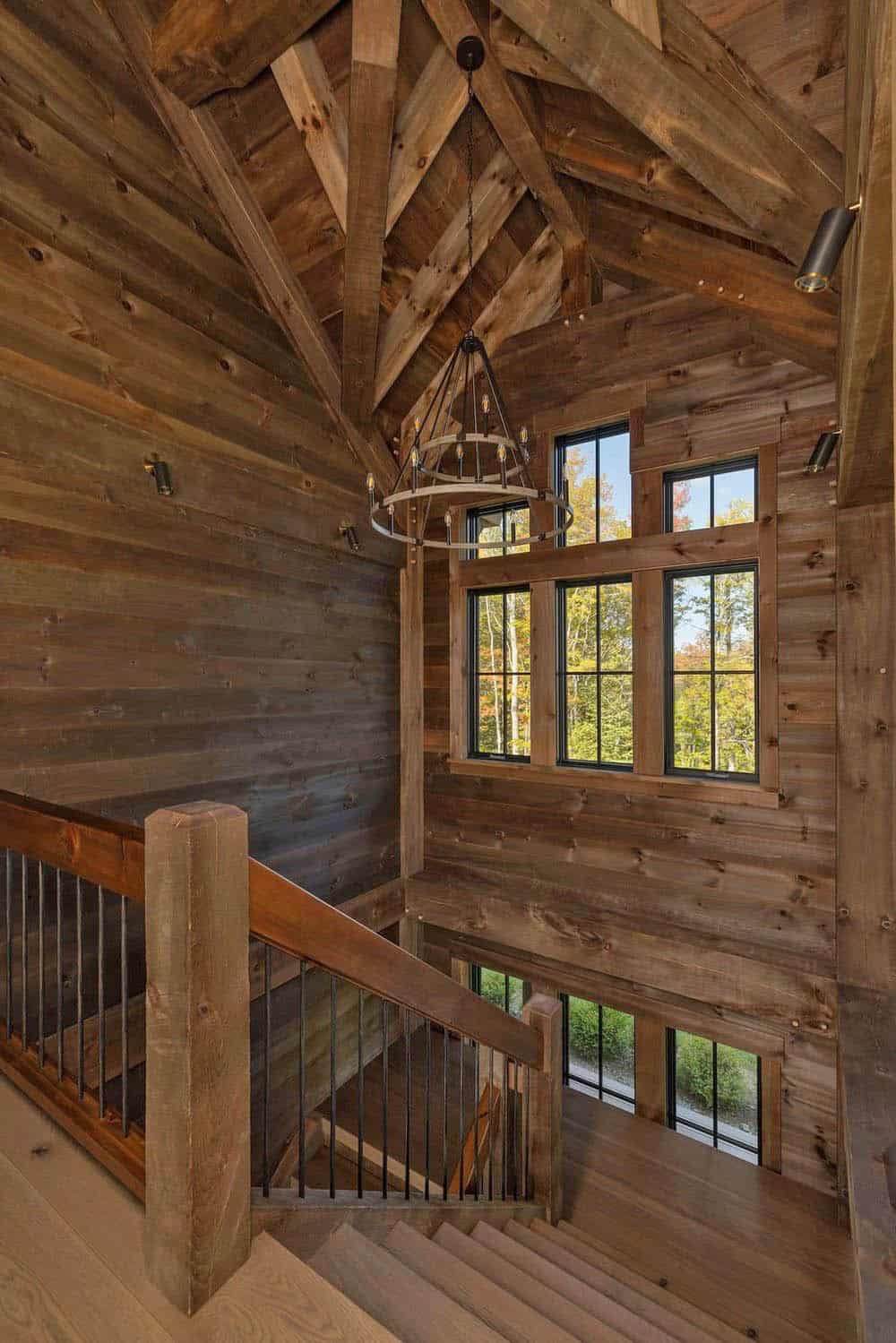 Stairwell with vaulted timber ceiling, wagon-wheel chandelier, and forest-view windows