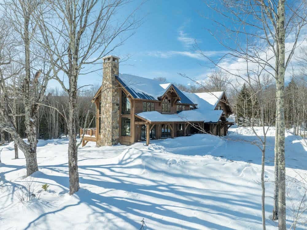 Timber frame mountain home exterior blanketed in snow with stone chimney