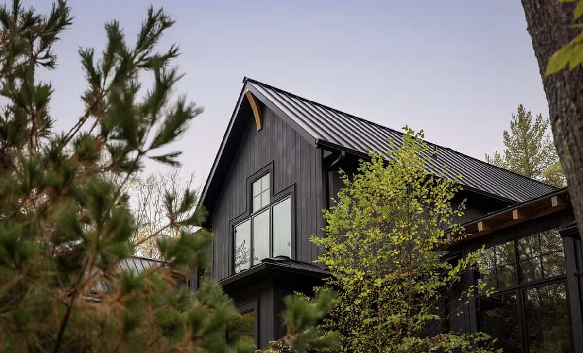 Close-up of black cottage gable with standing-seam metal roof and timber accent against a pale sky