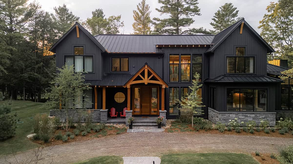 Front facade of black Muskoka cottage at dusk with glowing timber-framed entrance and red Adirondack chairs