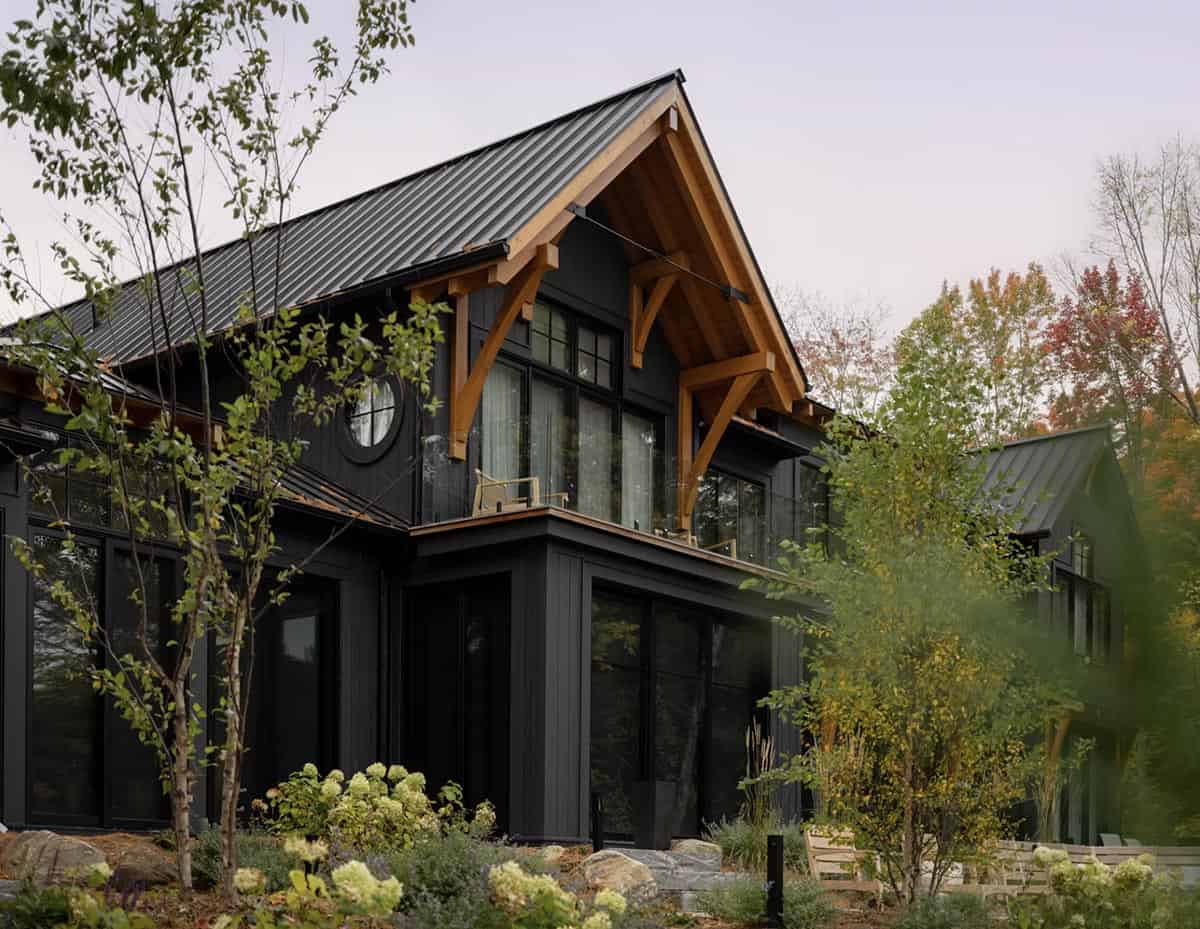 Lakeside gable of dark cottage featuring dramatic timber-frame arch, Juliet balcony, and floor-to-ceiling windows