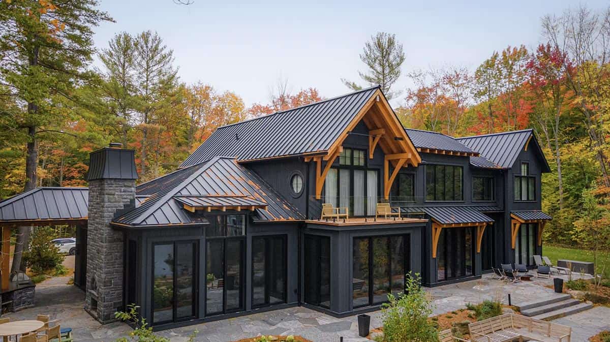 Aerial rear view of black Muskoka cottage with timber accents, wrap-around glazing, stone fireplace, and fall foliage