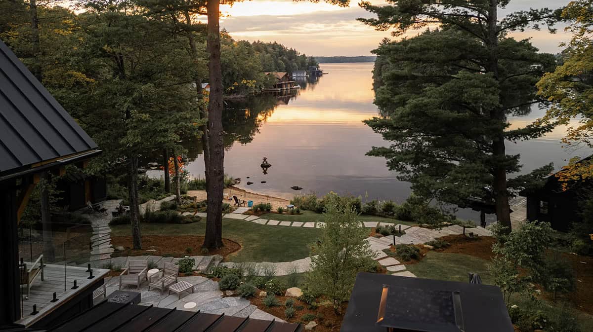 Sunset view of Lake Muskoka from a cottage deck with stone pathways, manicured grounds, and calm water reflections
