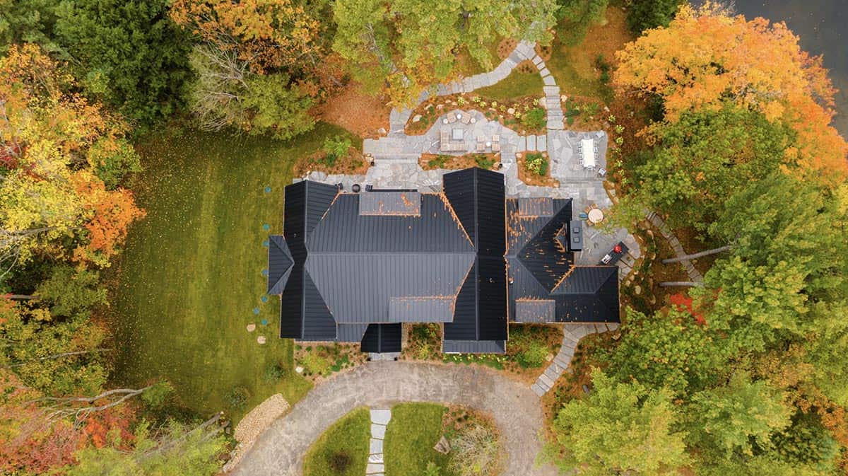 Top-down aerial view of cottage and landscaped grounds with stone terrace, fire pit, and peak fall foliage