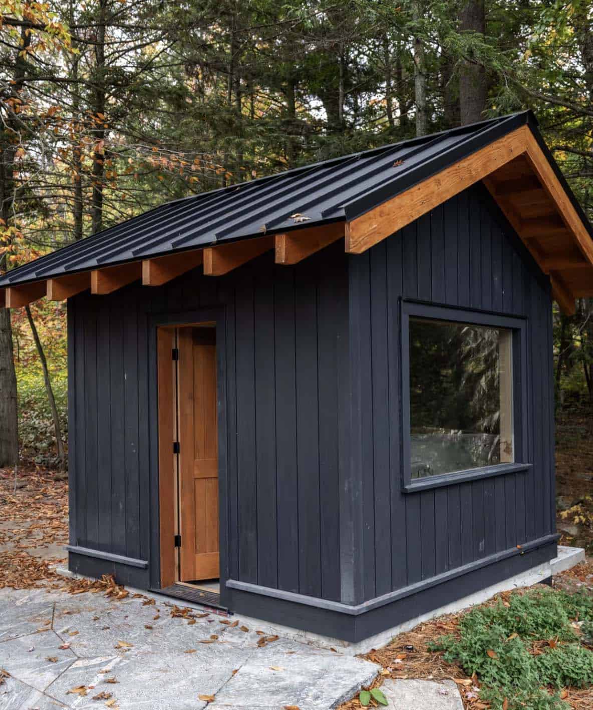 Compact black board-and-batten sauna outbuilding with timber gable detail and natural wood door