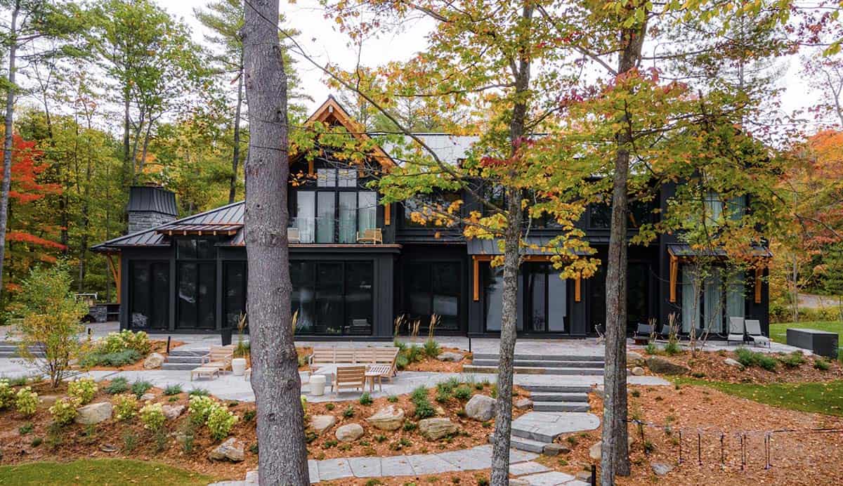 Rear exterior of Muskoka cottage with stone patio, timber pergola, large glazing, and colorful fall trees
