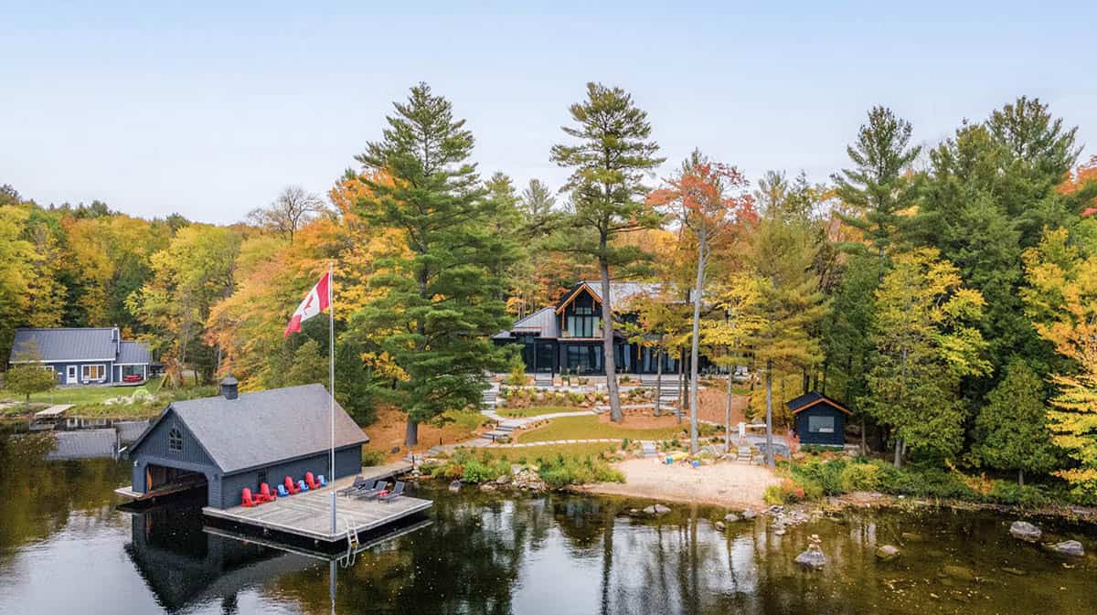 Waterfront view of cottage property with boathouse, Canadian flag, sandy beach, and autumn foliage