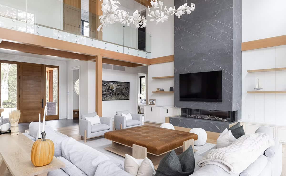 Soaring great room with double-height ceiling, white floral chandelier, floor-to-ceiling stone fireplace, and timber beams