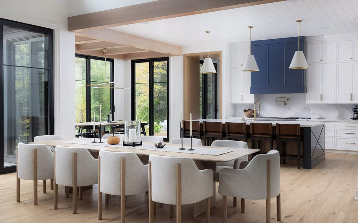 Dining area with oak table and boucl&eacute; chairs looking toward white and navy kitchen with brass pendant lights