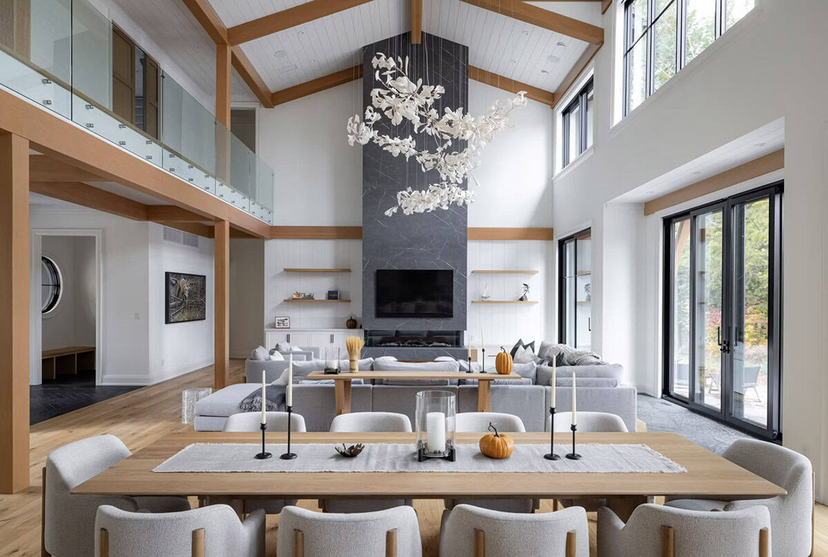 Bright great room with vaulted shiplap ceiling, timber frame, white floral chandelier, dining table, and stone fireplace