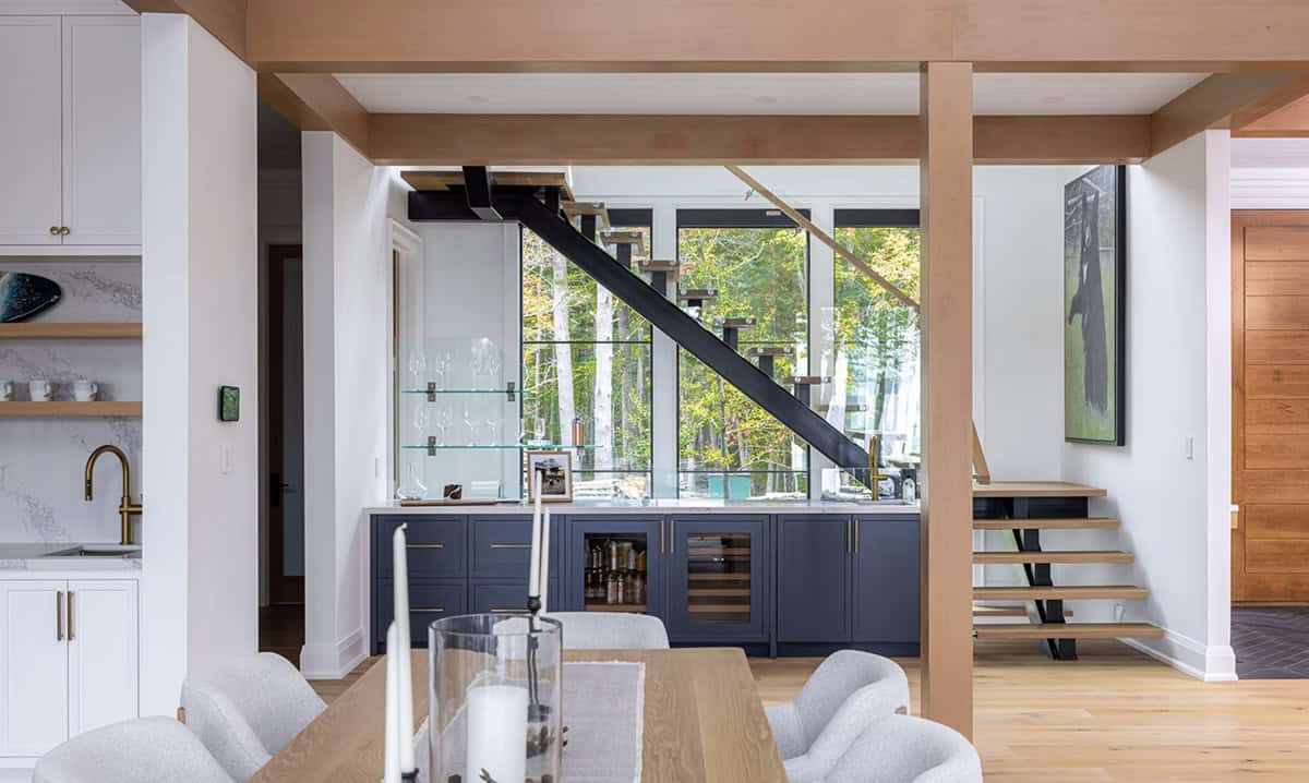 Butler's pantry with navy cabinets and wine fridge viewed through timber frame columns with floating staircase beyond