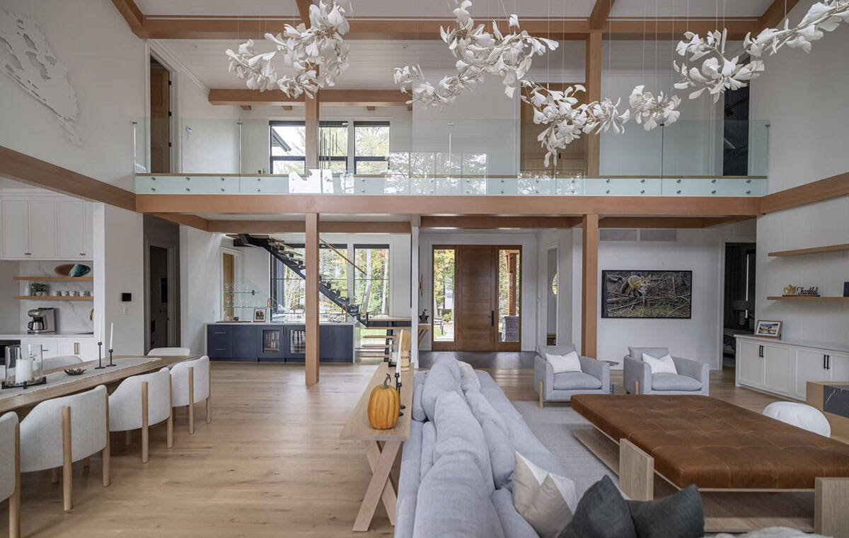 Grand open-plan cottage interior seen from lakeside end, with white floral chandeliers, timber posts, and wood front door