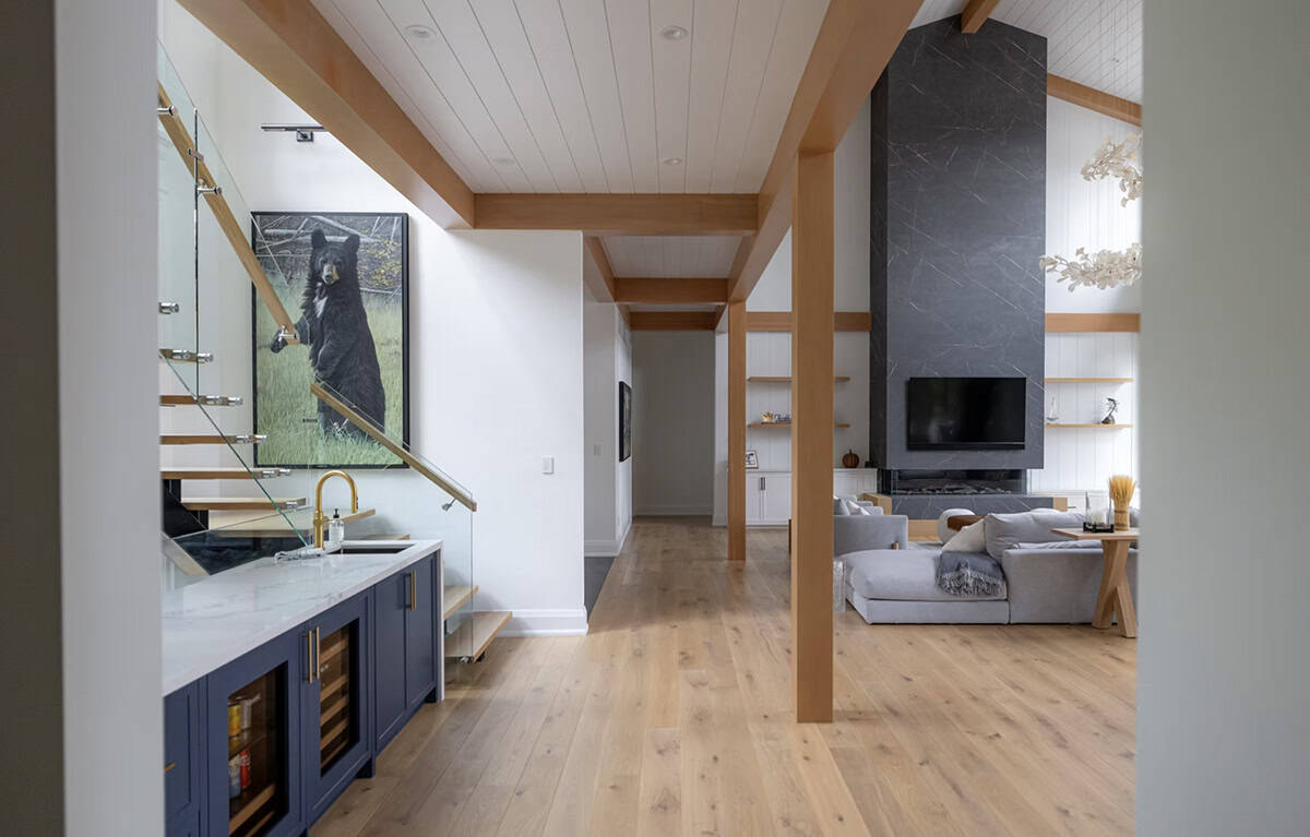 Hallway view from wet bar with navy cabinets through timber-framed corridor to stone fireplace living room
