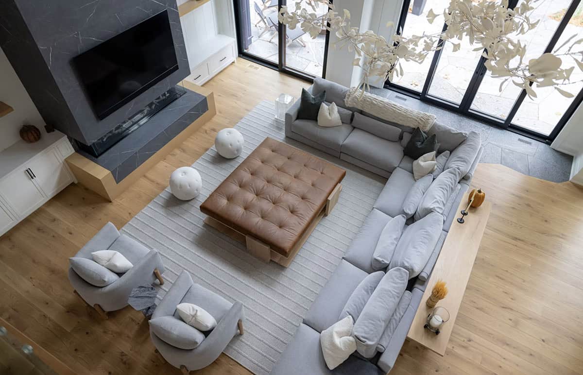 Overhead view of grey sectional seating arrangement around tufted leather ottoman with stone fireplace and black sliding doors