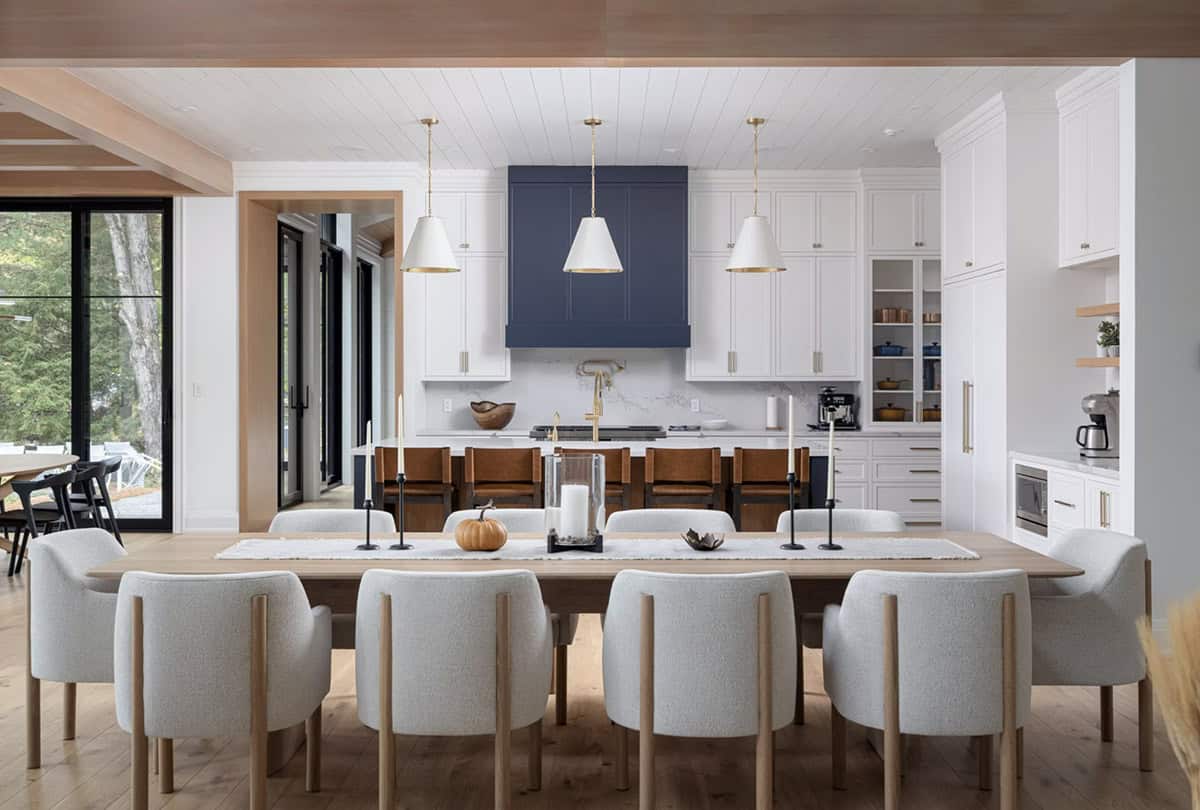 Dining table set with pumpkins looking straight into white and navy kitchen with brass pendant lights and island seating