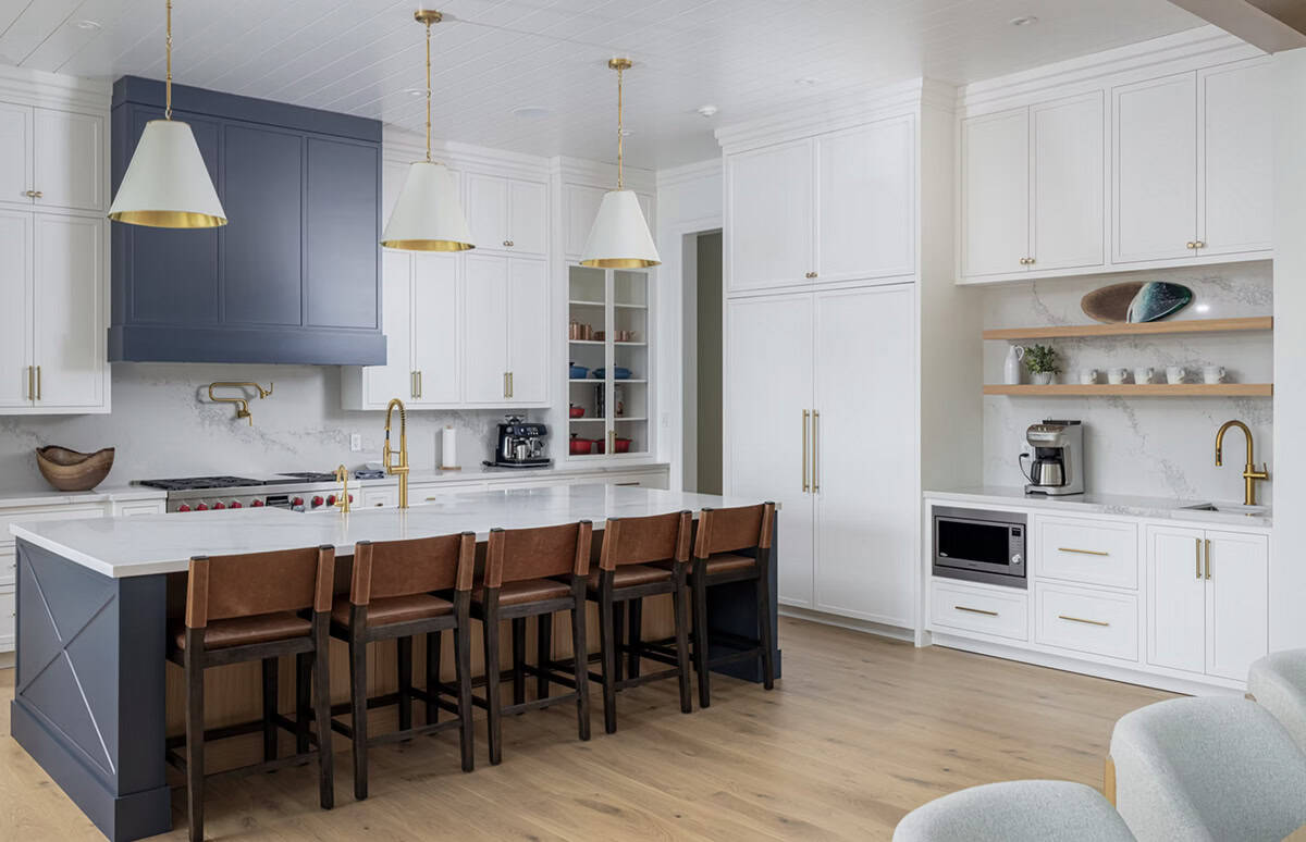 Navy kitchen island with leather bar stools, white upper cabinets, navy range hood, brass fixtures, and coffee station
