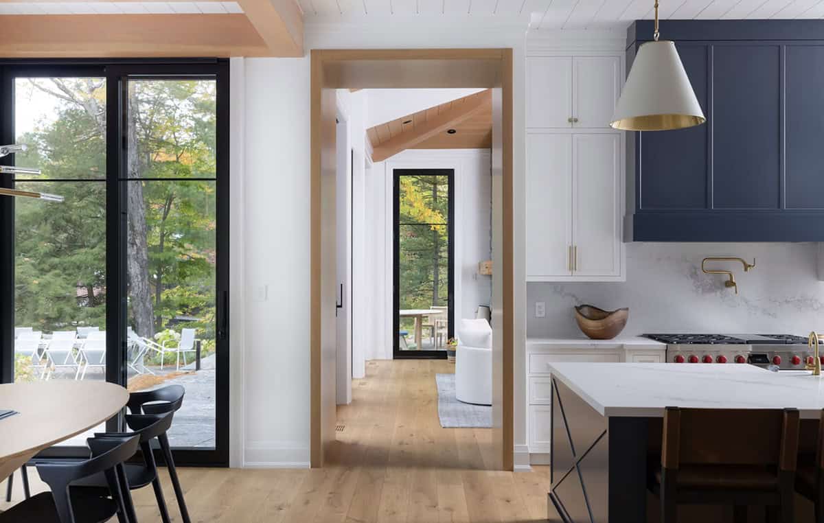 Kitchen passthrough with navy range hood and oak-framed doorway leading to bright sunroom with forest views