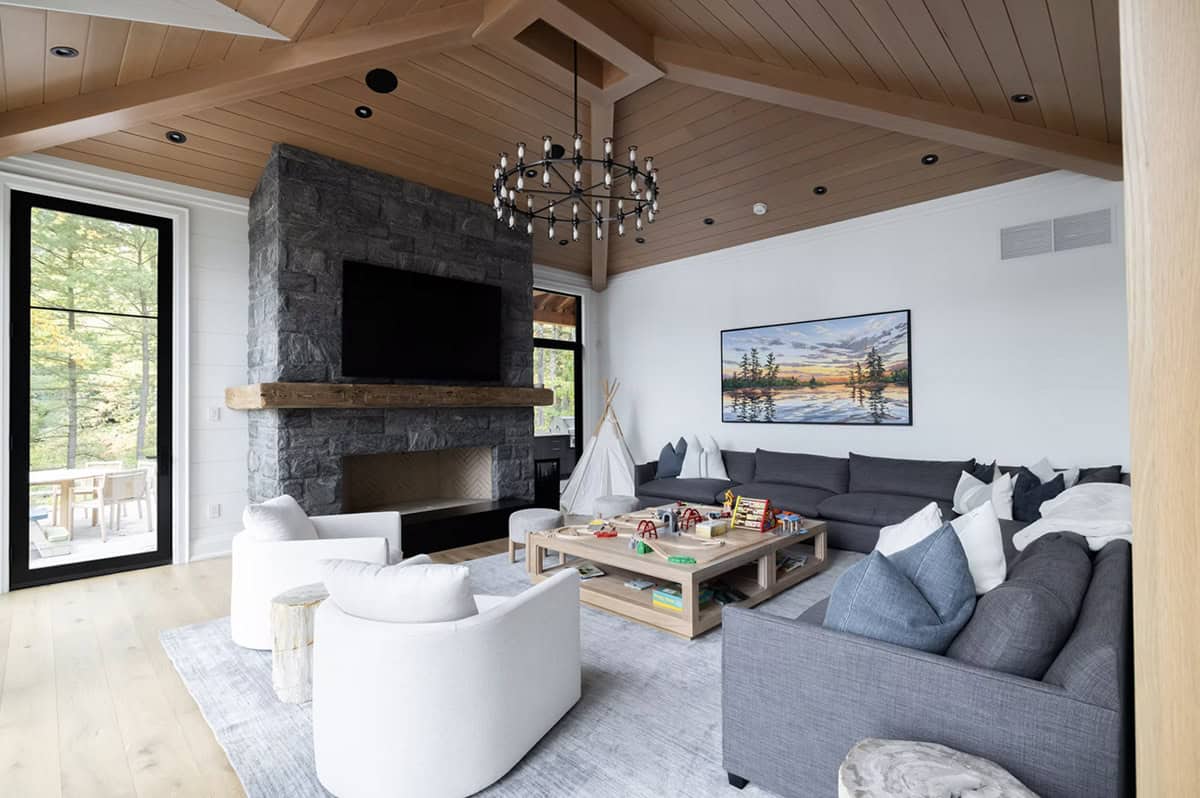 Family room with dark stone fireplace, reclaimed wood mantel, cedar ceiling, iron chandelier, and grey sectional sofa