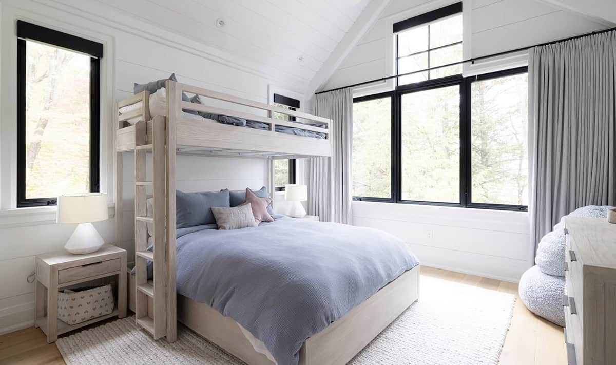 Children's bedroom with whitewashed bunk bed, blue bedding, vaulted shiplap ceiling, and large black-framed windows