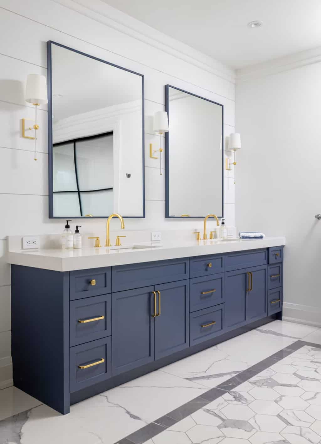 Guest bathroom double vanity with navy cabinets, brass faucets and hardware, square navy-framed mirrors, and marble hex floor tile