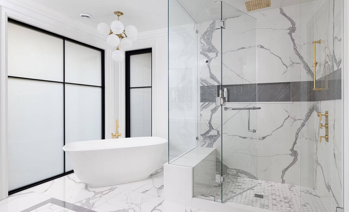 Luxurious bathroom with freestanding white soaker tub, brass freestanding filler, glass-enclosed marble shower, and globe chandelier
