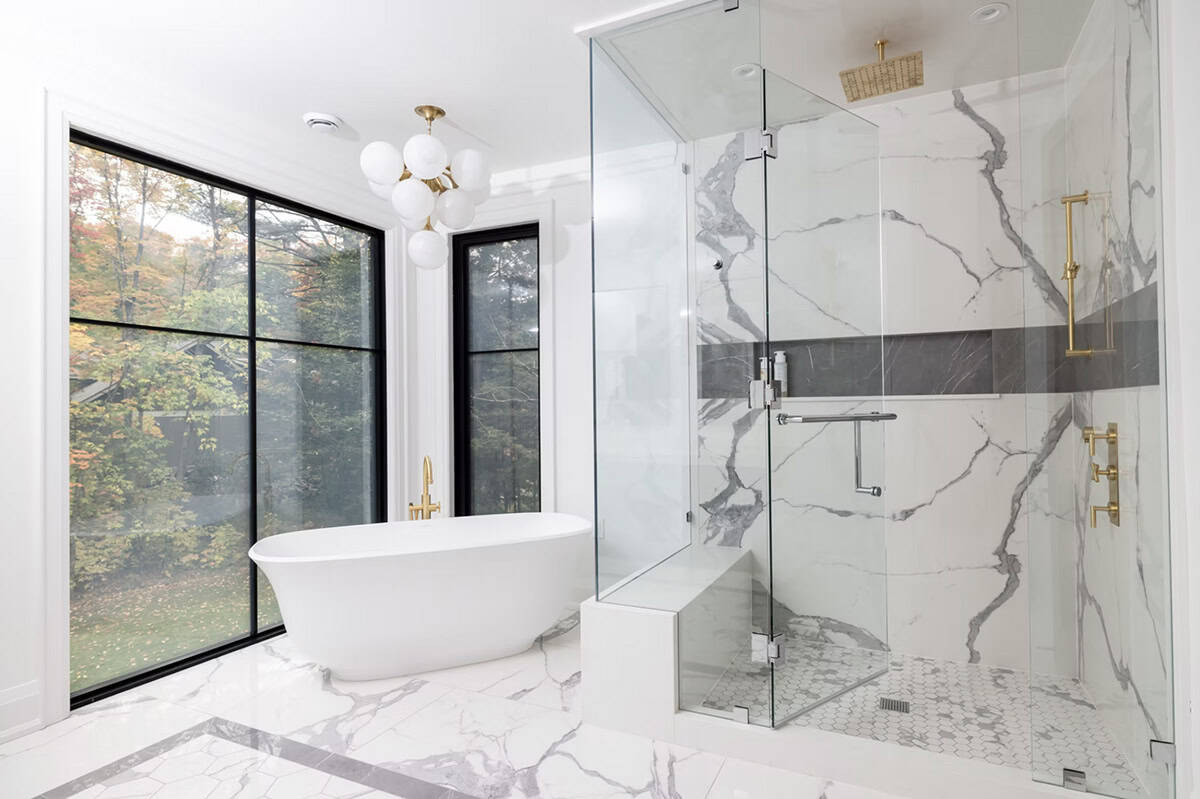 Bathroom with white freestanding tub, brass fixtures, full-height marble shower enclosure, hexagonal floor tile, and globe chandelier
