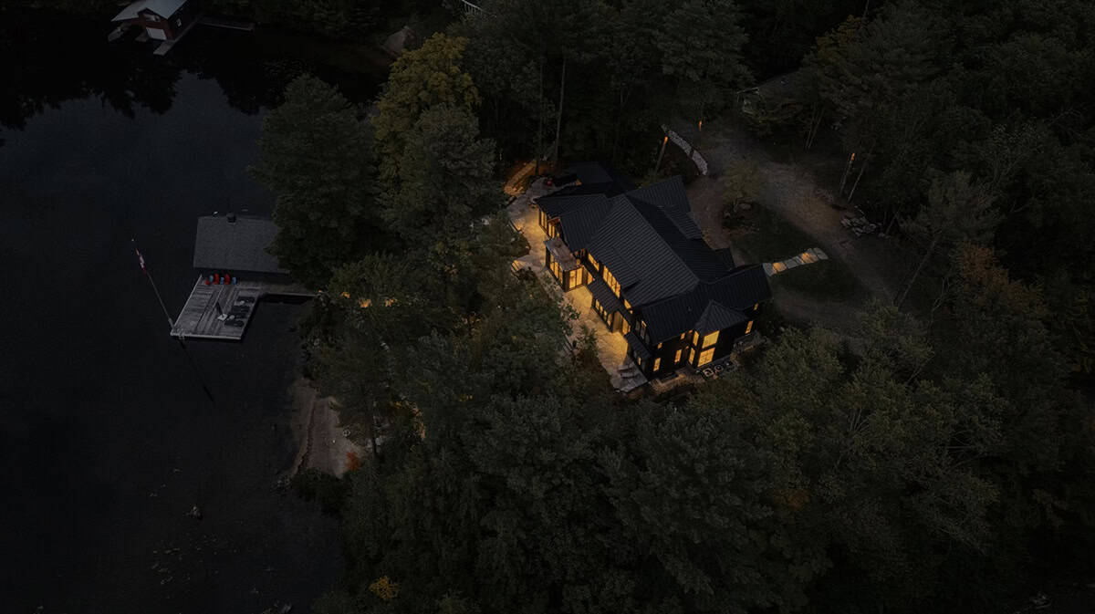 Nighttime aerial view of lit cottage and boathouse compound on Muskoka lakefront surrounded by dark forest