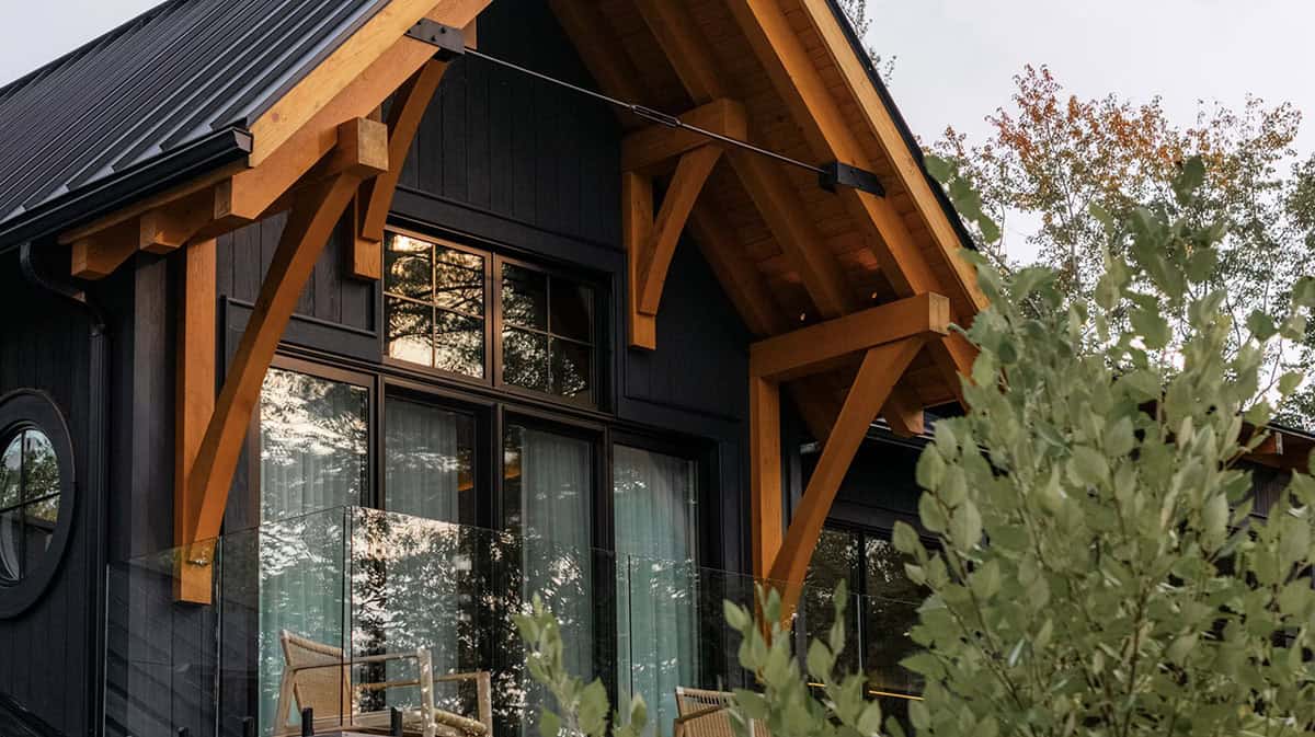 Close-up of timber-frame gable arch on black cottage exterior with balcony chairs and porthole window at dusk