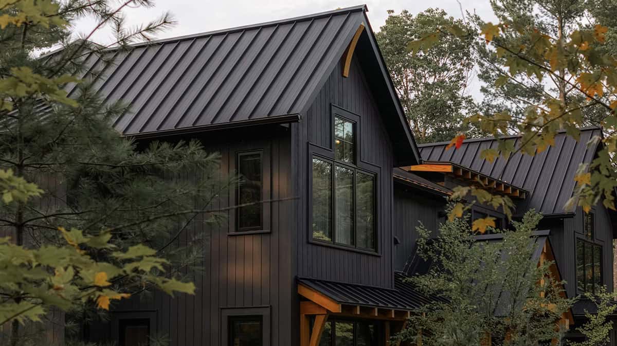 Detail of black board-and-batten cottage gable with curved timber accent and standing-seam metal roof amid fall foliage