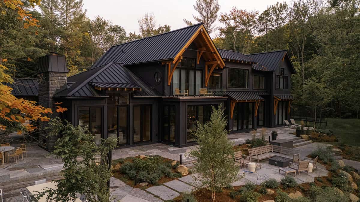 Rear aerial view of black cottage with timber-framed balcony, wraparound stone patio, fire pit seating, and stone outdoor fireplace