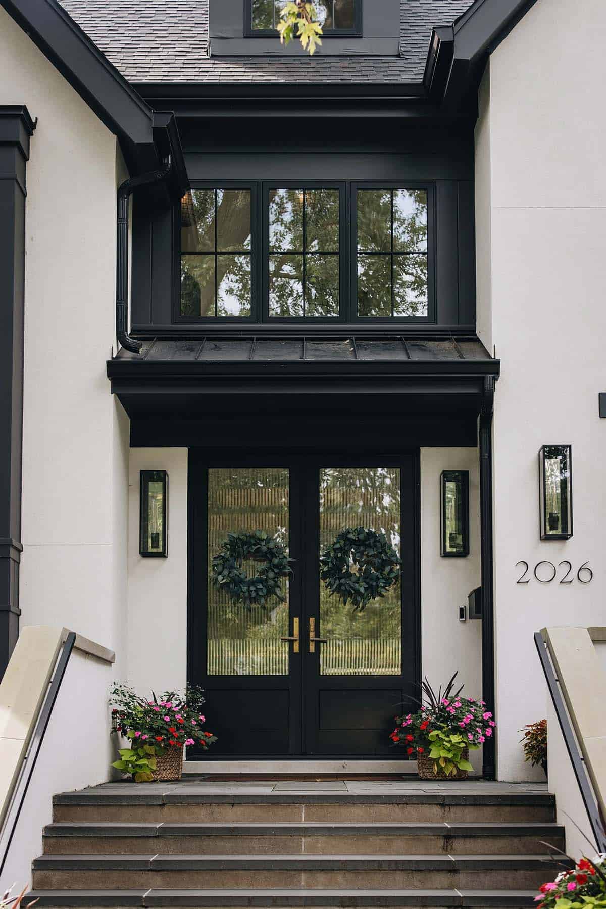 Close-up of black double entry doors with reeded glass panels, brass hardware, and flanking wall sconces on a white stucco facade