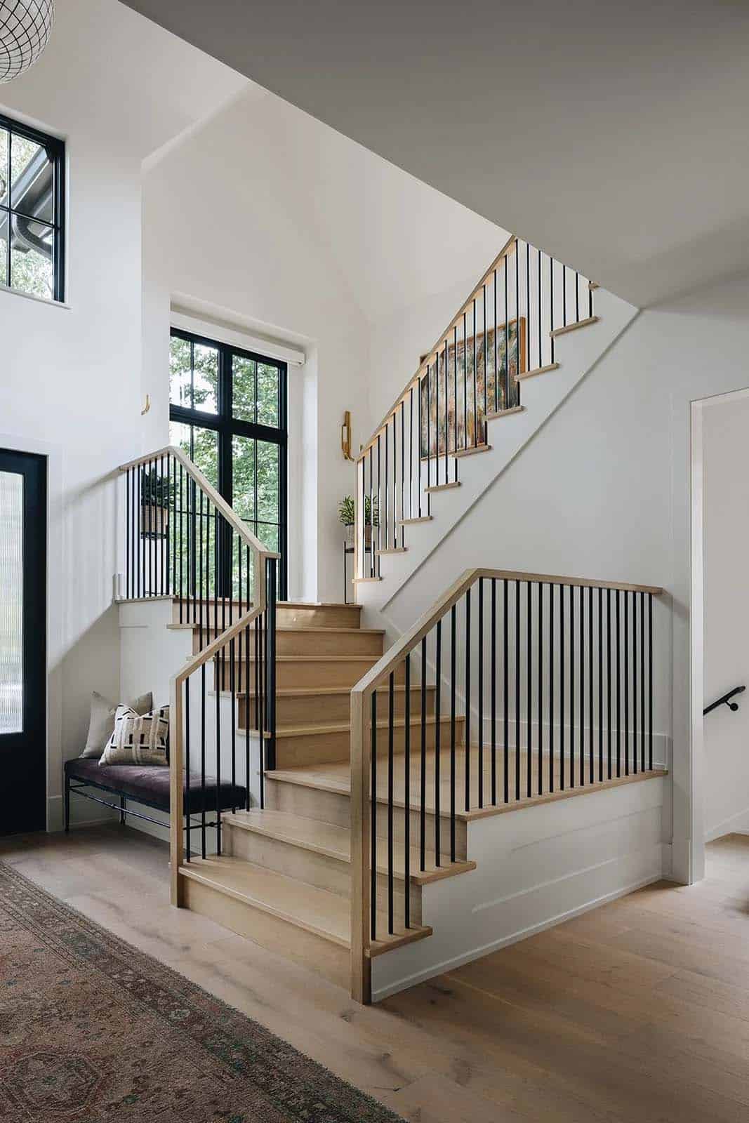 Open floating staircase with natural oak steps, black metal spindles, and a two-story window wall flooding the entry with natural light
