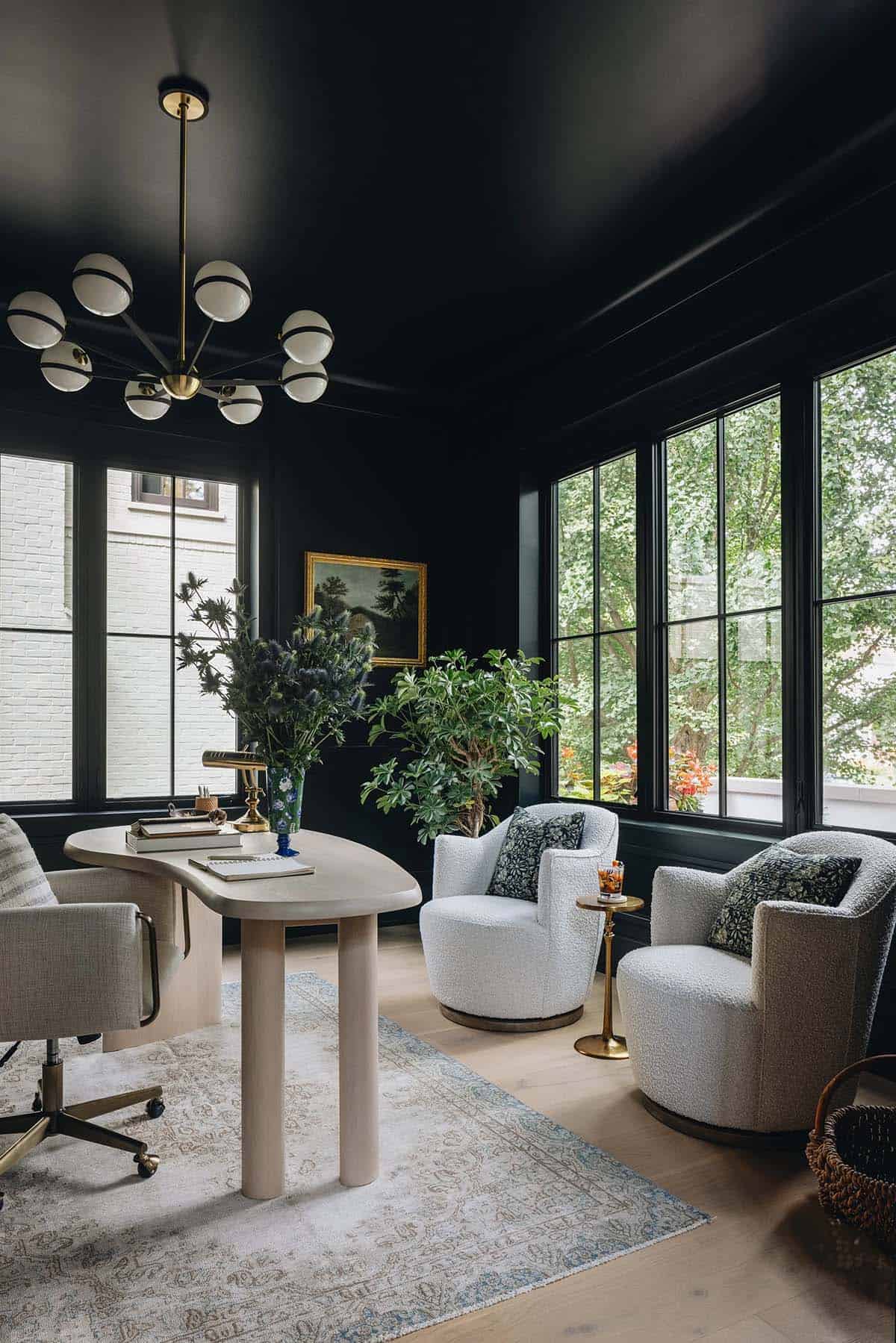 Moody home office with black walls, oversized grid windows, boucle swivel chairs, and a sculptural plaster desk centered on a vintage rug