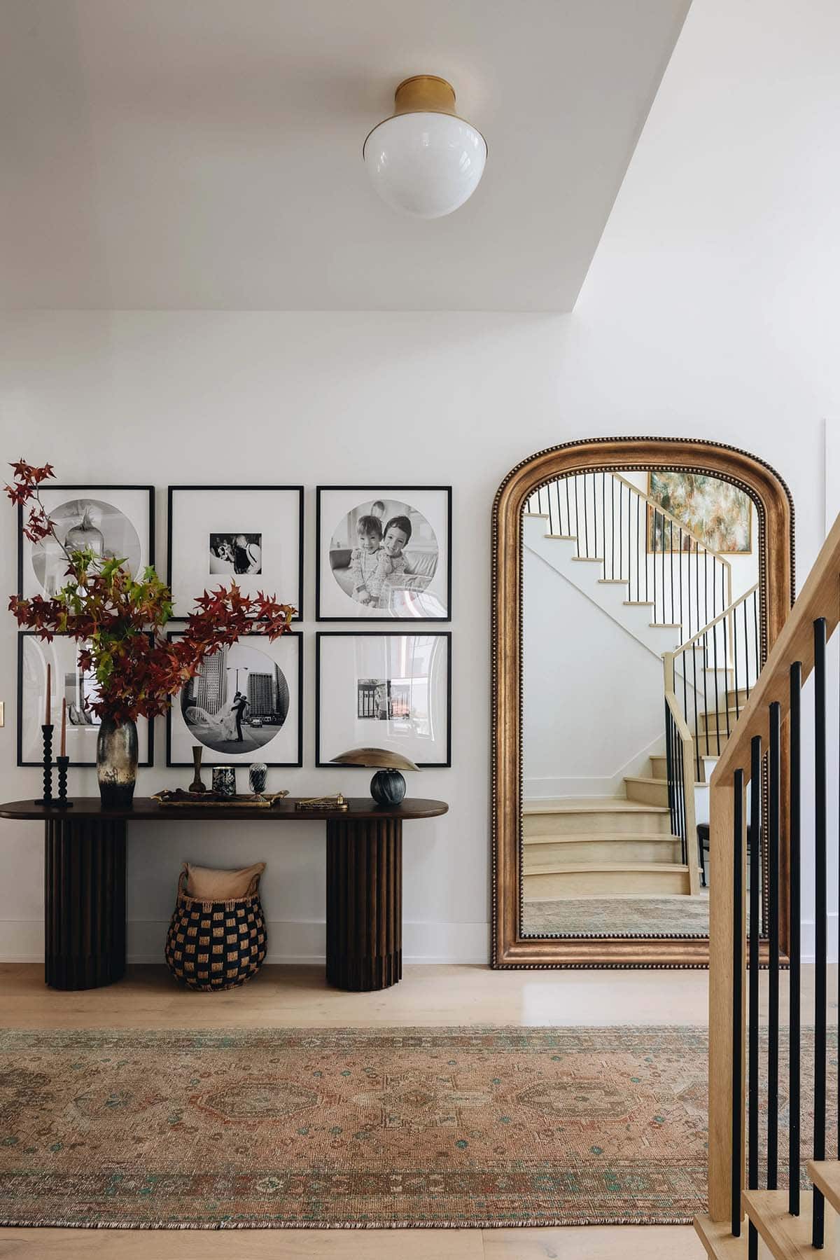 Hallway vignette with dark wood fluted console table, black-framed gallery wall of family photos, and a large arched gilt mirror