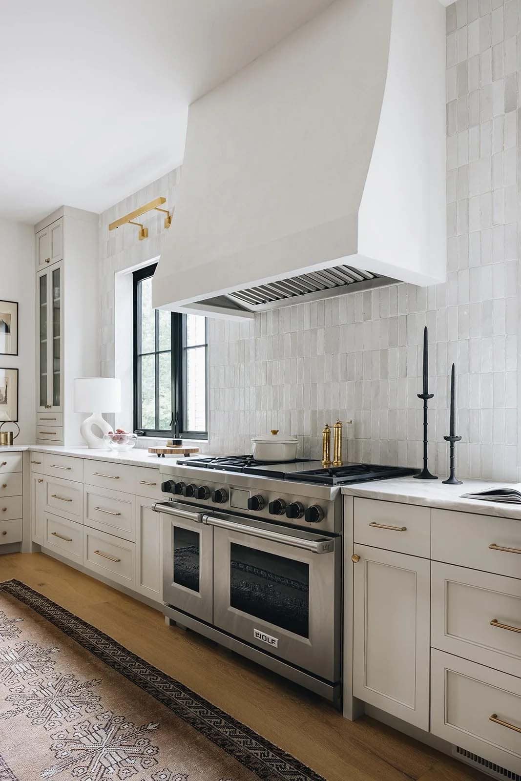 Kitchen cooking wall with Wolf range, zellige tile backsplash, white plaster hood, cream shaker cabinets, and brass hardware