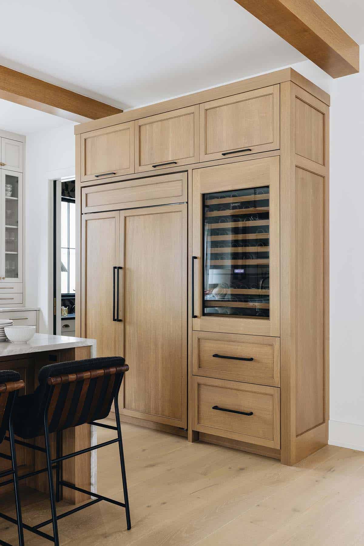 Tall natural oak refrigerator cabinet panel with integrated wine cooler, black hardware, and matching oak upper cabinets