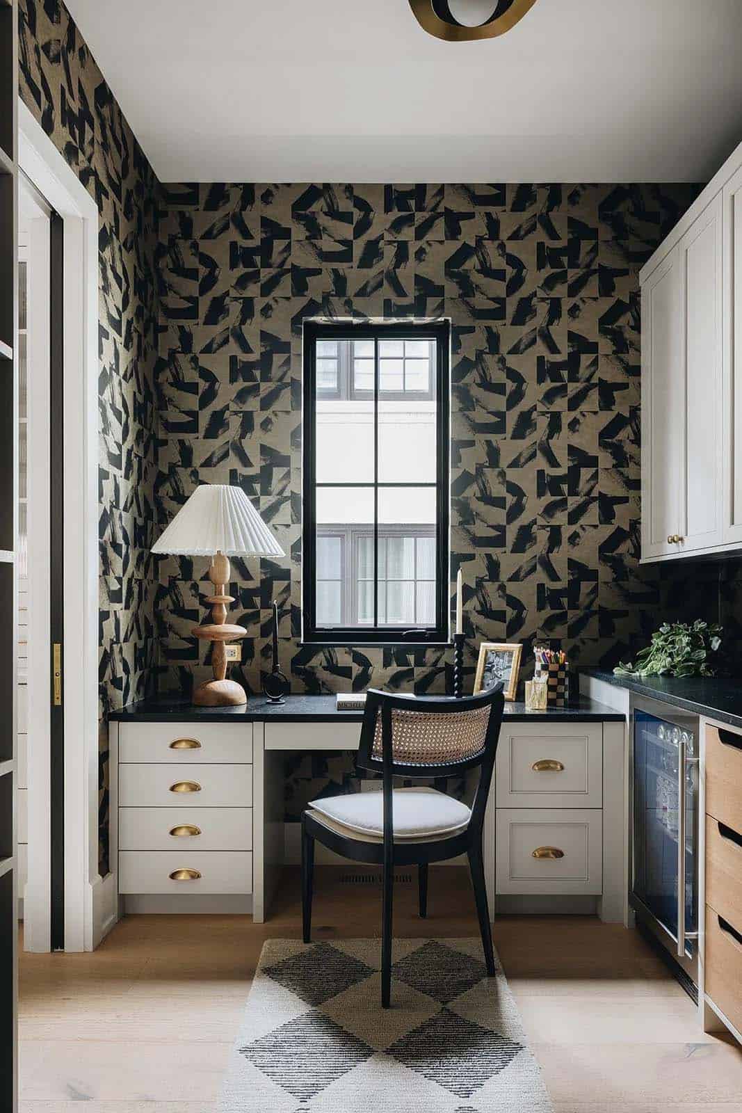 Butler's pantry with bold graphic black and tan wallpaper, built-in desk, black granite countertop, cane-back chair, and a pleated lamp on a sculptural wood base