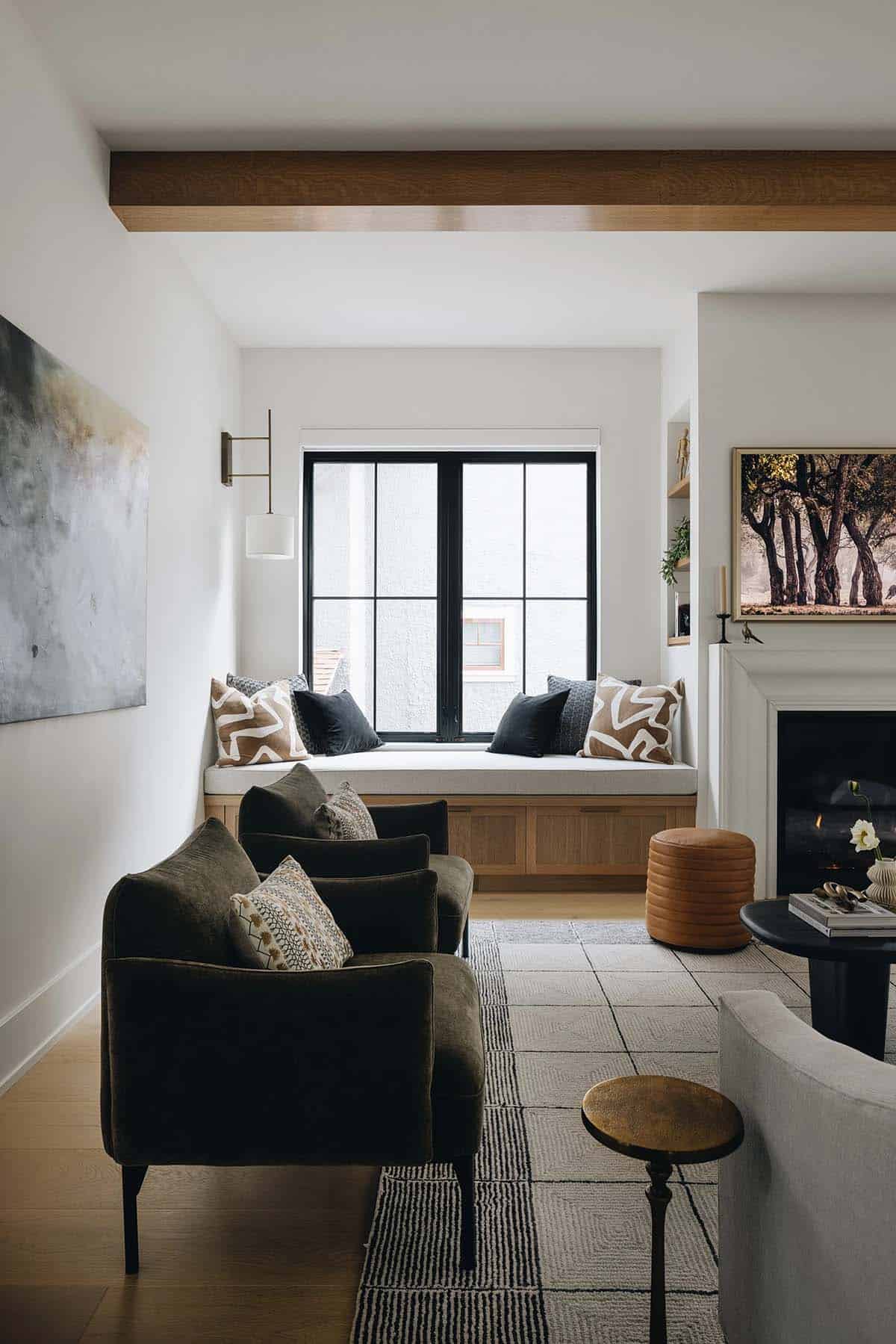Living room with oak ceiling beam, built-in window seat, dark olive velvet armchairs, a fireplace, and a large landscape painting above the mantel