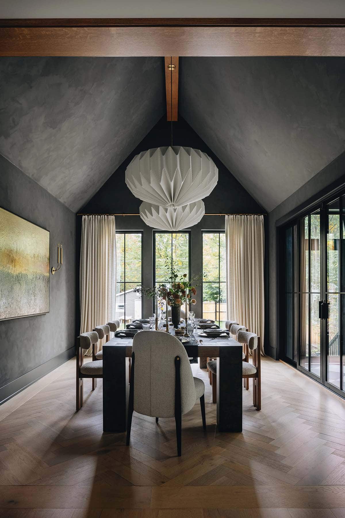 Formal dining room with vaulted plaster ceiling, paired oversized origami pendants, dark oak table with boucle chairs, and floor-to-ceiling black-framed windows